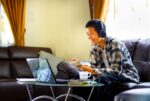 A high school senior wearing headphones works on his homework from a laptop.